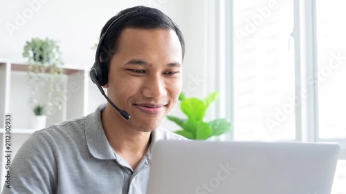 Indonesian business man speaking having virtual meeting on laptop. Wearing headset talking consulting on video call at home office call center.