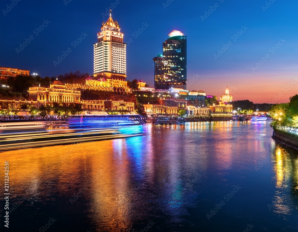Fototapeta premium illuminated cityscape and river cruise at dusk reflecting colorful lights on water