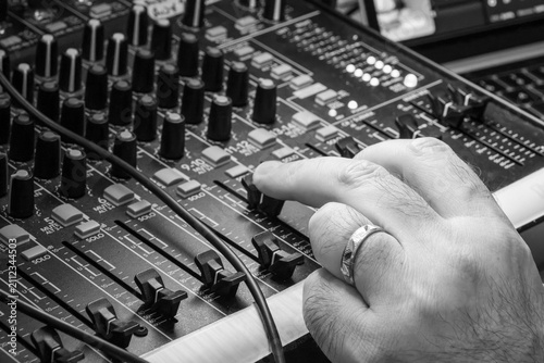 Close-up of a hand adjusting a knob on a black and white audio mixing console in a studio. Professional sound engineer working on a monochrome music mixer board.