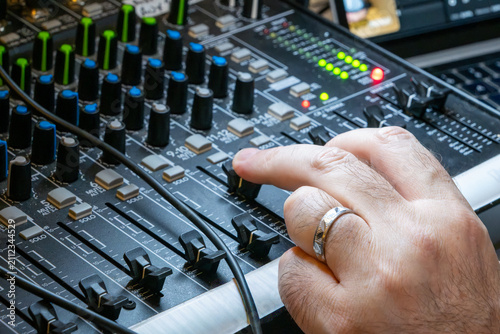 Close-up of a hand adjusting a knob on an audio mixing console in a studio. Sound engineer working on a professional music mixer board, live sound production concept.