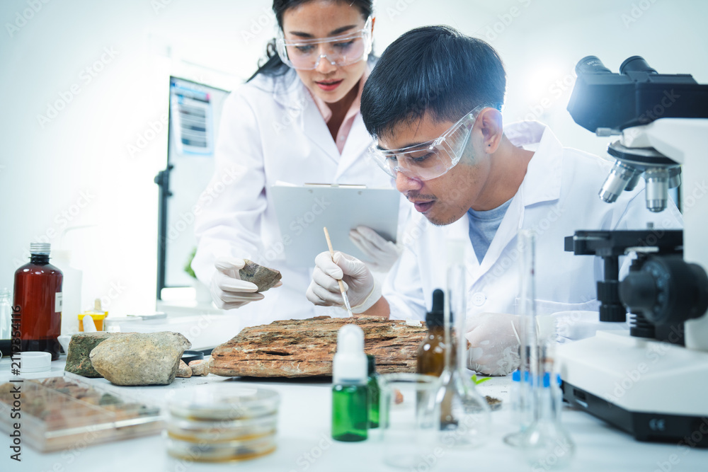 Fototapeta premium Laboratory scientist microscope rock research safety eyewear analysis mineral sample, focused team examine stone with tool, glassware, chemical bottle, bright science workspace
