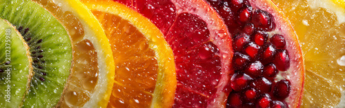 Colorful slices of citrus and fruits show different types of fruit cut and arranged on a table with water droplets on them
