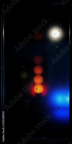Blurred city lights behind rain covered glass at night