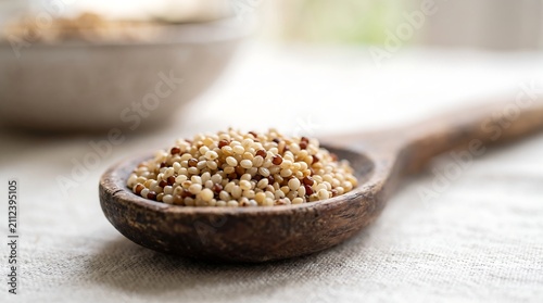 Close up view of uncooked mixed quinoa grain in wooden spoon on white cloth background.