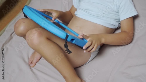 A child plays on a bright blue tablet while resting it on their knees indoors. They feel curious and happy during a moment of joyful, focused entertainment.