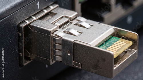Close up of a metallic sfp optical transceiver module with exposed gold pins plugged into a telecommunications network switch