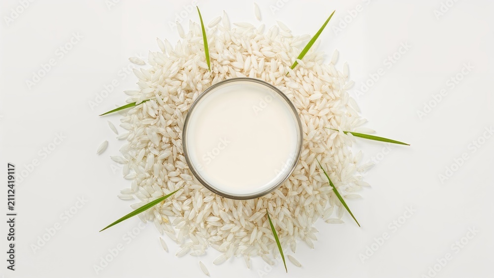Obraz premium A glass of milk surrounded by rice grains and green leaves arranged in a circular pattern.