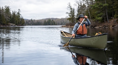 Female canoeist paddling on calm lake with forest background  