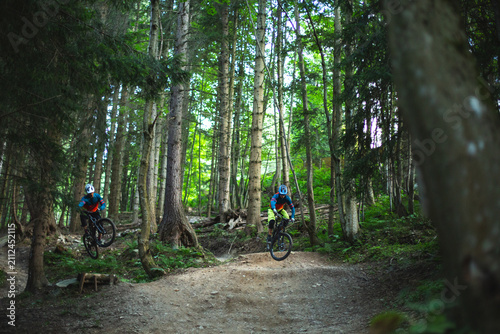 Two mountain bikers riding enduro bikes through a bike park trail,