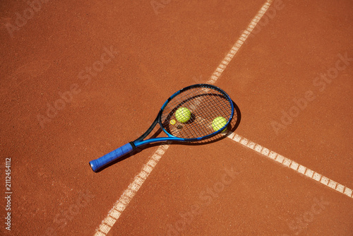 Tennis Racket and Balls on Clay Court During a Sunny Day