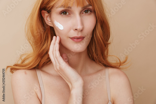 Bild auf Leinwand Calm portrait of a woman applying white cream to her cheek, soft lighting, smoot