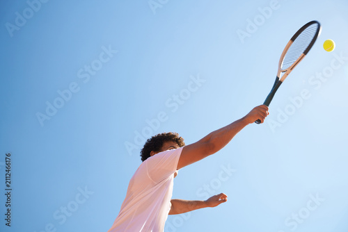 Tennis Player Serves Ball Under Clear Blue Sky During Daytime