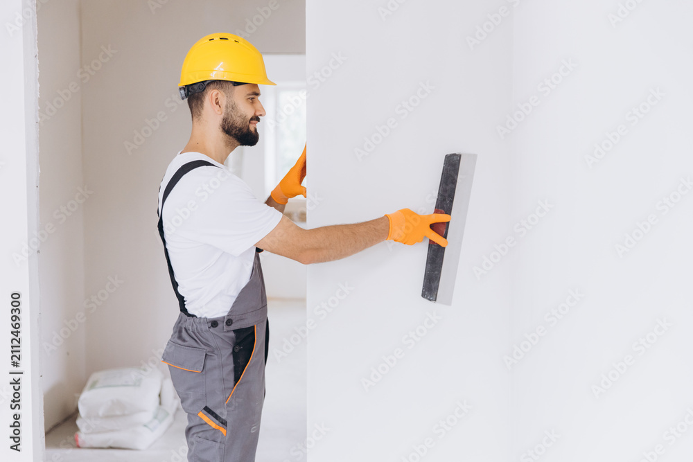 Obraz premium Manual worker plastering a wall in a room during home renovation, preparing surface finish for painting