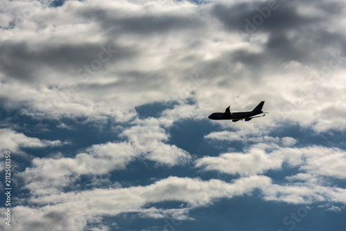 Fotografie Silhouette of commercial jet airliner flying against dramatic backlit clouds in