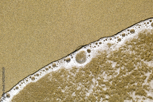 Fotografie Minimalist wave and sea foam dividing dry and wet sand on beach