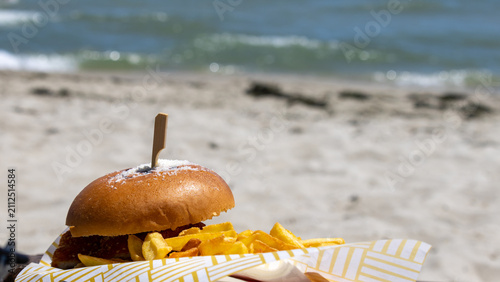 Delicious burger and french fries served on a beach with sea background