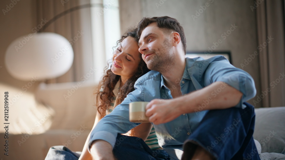 Obraz premium Smiling couple cuddling coffee cups sofa. Affectionate pair relaxing weekend