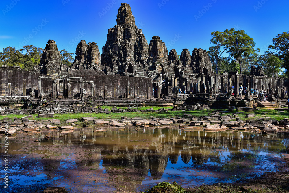Naklejka premium Bayon Temple with its iconic stone face towers reflected in water at Angkor Thom near Siem Reap, Cambodia, showcasing the ancient architecture and cultural heritage of the Khmer Empire.