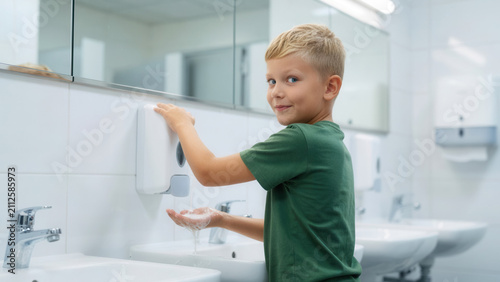 Child boy washing hands in school bathroom at white sink, hygiene and health education for children