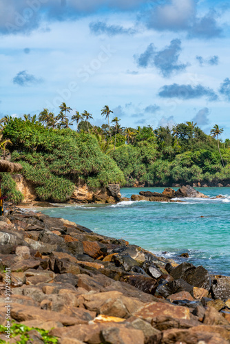 Large rock formations sticking out of crashing ocean waves near Ahangama Beach, Sri Lanka. Scenic seascape with rocky shoreline and sea foam in turquoise Indian Ocean, Ahangama, Sri Lanka. 