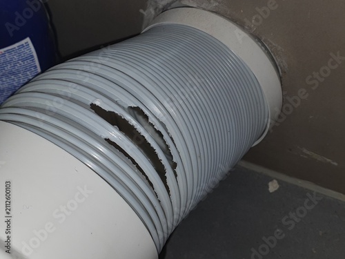 A close-up view of a damaged gray flexible corrugated ventilation hose or duct pipe showing a large tear and split in the ribbed plastic material. The flexible tubing appears to be connected to a