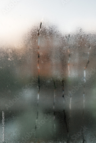 Condensation-covered window with water streaks illuminated by warm morning sunlight, creating an abstract seasonal background.