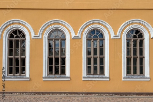 A row of four arched windows with white trim set into a yellow historic building facade. An architectural stock photograph captured during the daytime in Ventspils, Latvia.