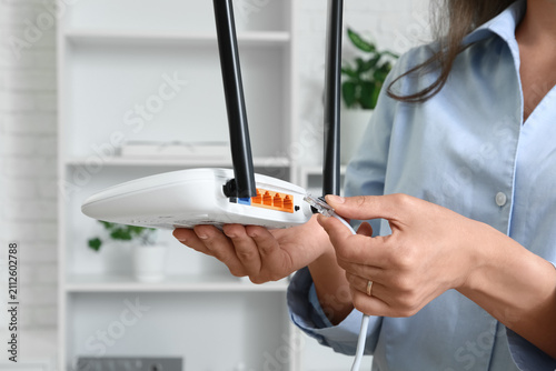 Obraz na płótnie Woman connecting an ethernet cable to a white wireless router for internet acces