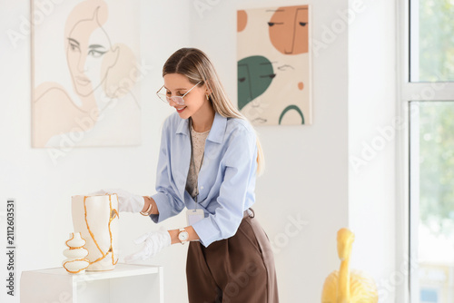 Принти на полотні Young female art gallery curator wearing white gloves carefully arranging kintsu