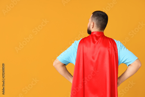 Young man dressed as superhero on orange background, back view