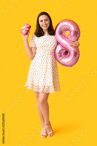 Beautiful young woman with pink air balloon in shape of figure 8 and gift box...