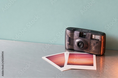 Disposable camera with two developed photographs on a metallic table. Retro photography equipment for film capturing. Analog nostalgia concept, vintage hobby and capture memories.