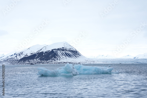 Foto Blue iceberg floating in the cold Arctic ocean with snowy mountains in Svalbard