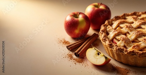 Fresh baked apple pie sits near cinnamon sticks, whole red fruit on table. Golden light illuminates pastry crust with sweet filling. Composition provides wide negative space on beige background for