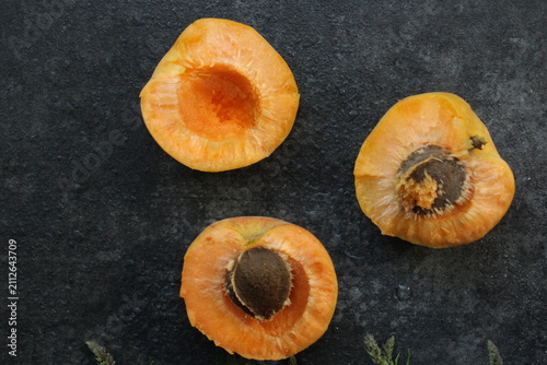 Obraz na plátně Three fresh apricot halves with pits on a dark textured stone background, captured in a minimalist flat lay composition with natural lighting