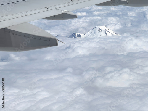 airplane wing and aerial view of heavy cloud cover and mostly snow-covered peak of Mt. Baker in Mt. Baker-Snoqualmie National Forest, National Park, viewed from a jet in July 2026