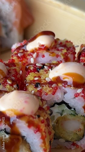 Fresh sushi rolls topped with bright red tobiko creamy japanese mayonnaise and unagi sauce arranged on a wooden serving board with avocado