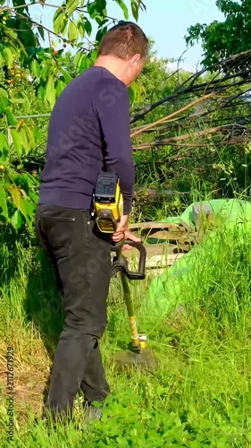 Keeping the property neat and well maintained, he carefully cuts the grass around fruit trees. The scene reflects seasonal garden care, outdoor work and a peaceful countryside lifestyle.