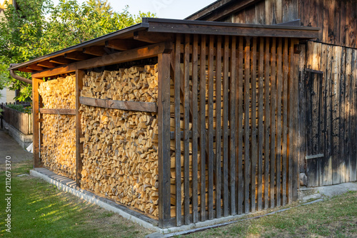 Neatly stacked firewood stored under wooden shelter beside traditional countryside building