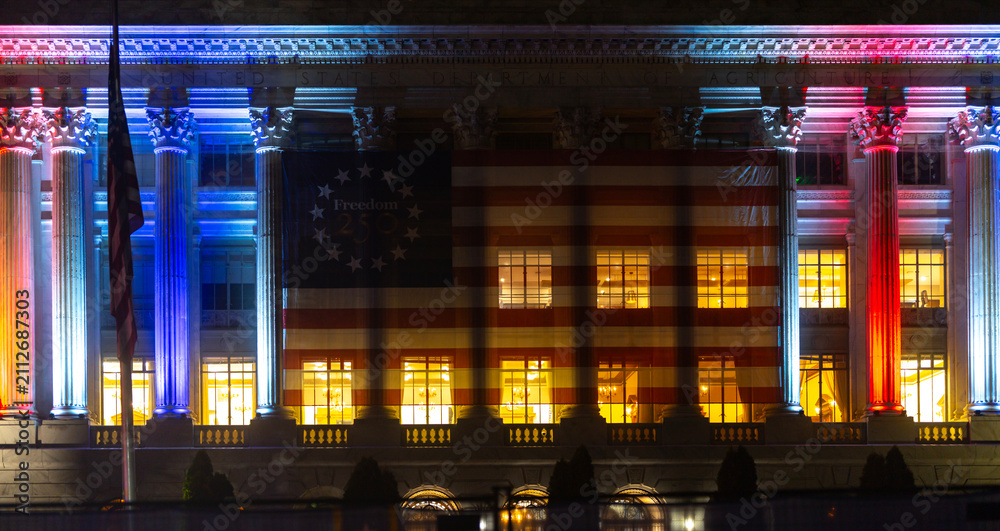 Obraz premium America flag covers federal building. America anniversary lights historic facade. Patriotic banner marks America freedom. Government columns frame America celebration.