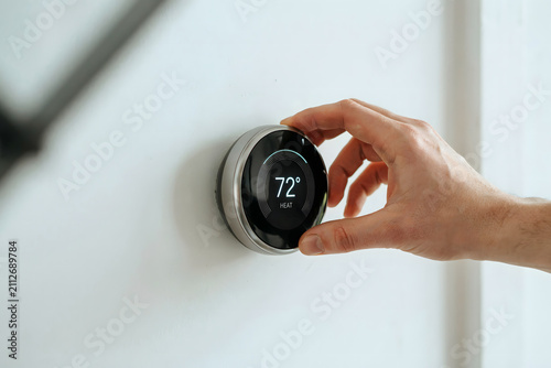 Close up of a hand rotating the outer ring of a round smart thermostat on a white wall to set the temperature to seventy-two degrees