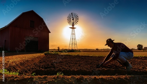 silhouettefarmer planting in a field windmill and barn in background