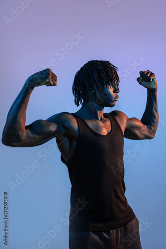 African man flexing muscular arms in blue studio light