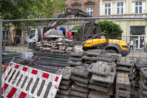 Fotografie A construction site behind a metal mesh fence, a yellow and black excavator
