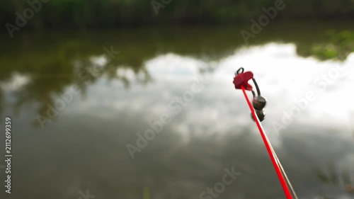 Bell bite indicator attached to fishing rod moving after fish strike near waterside. Concept of sport fishing and freshwater angling