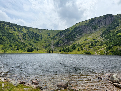 Scenic Mały Staw Mountain Lake in the Karkonosze Mountains with Crystal Water, Green Slopes and Dramatic Summer Sky