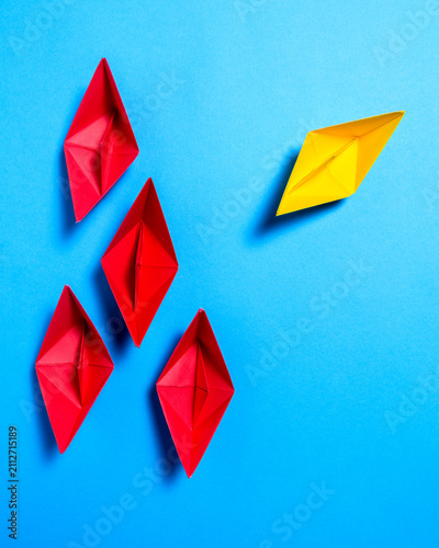 Yellow Paper Boat Moving Away From Red Paper Boats On Blue Background