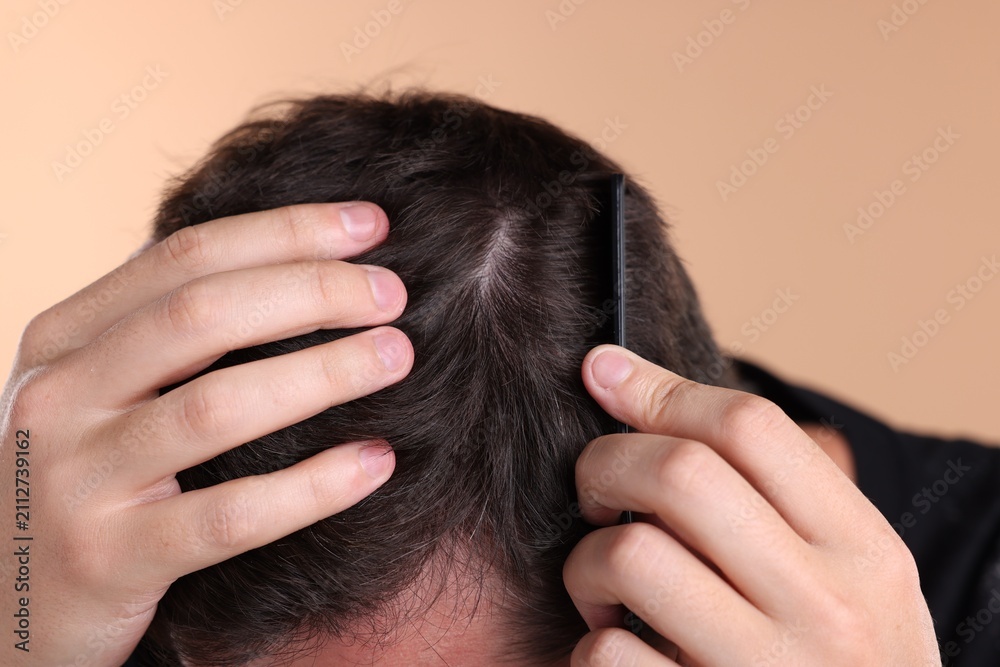 Fototapeta premium Man combing his hair on beige background, closeup
