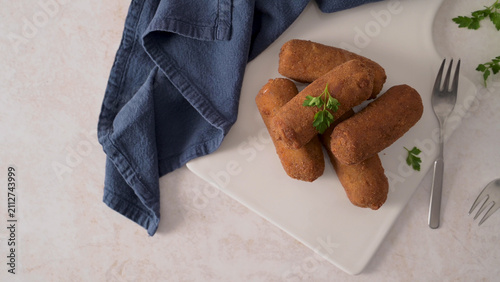 Crispy fried croquettes on a white plate with a blue cloth