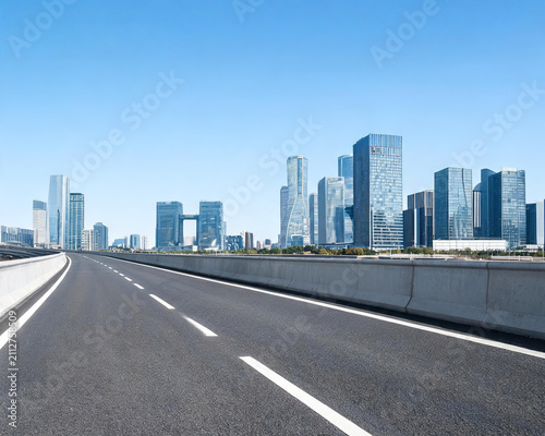 An empty asphalt highway stretches toward a modern city skyline of glass skyscrapers under a clear blue sky.